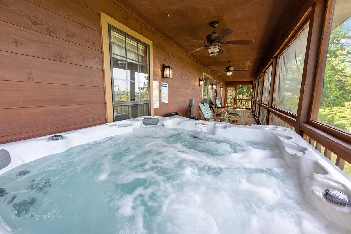 A screened porch interior with a hot tub, wooden walls, and ceiling fans, blending indoor relaxation with the fresh mountain air. The space exudes tranquility and offers a blend of privacy and resort-style comfort.