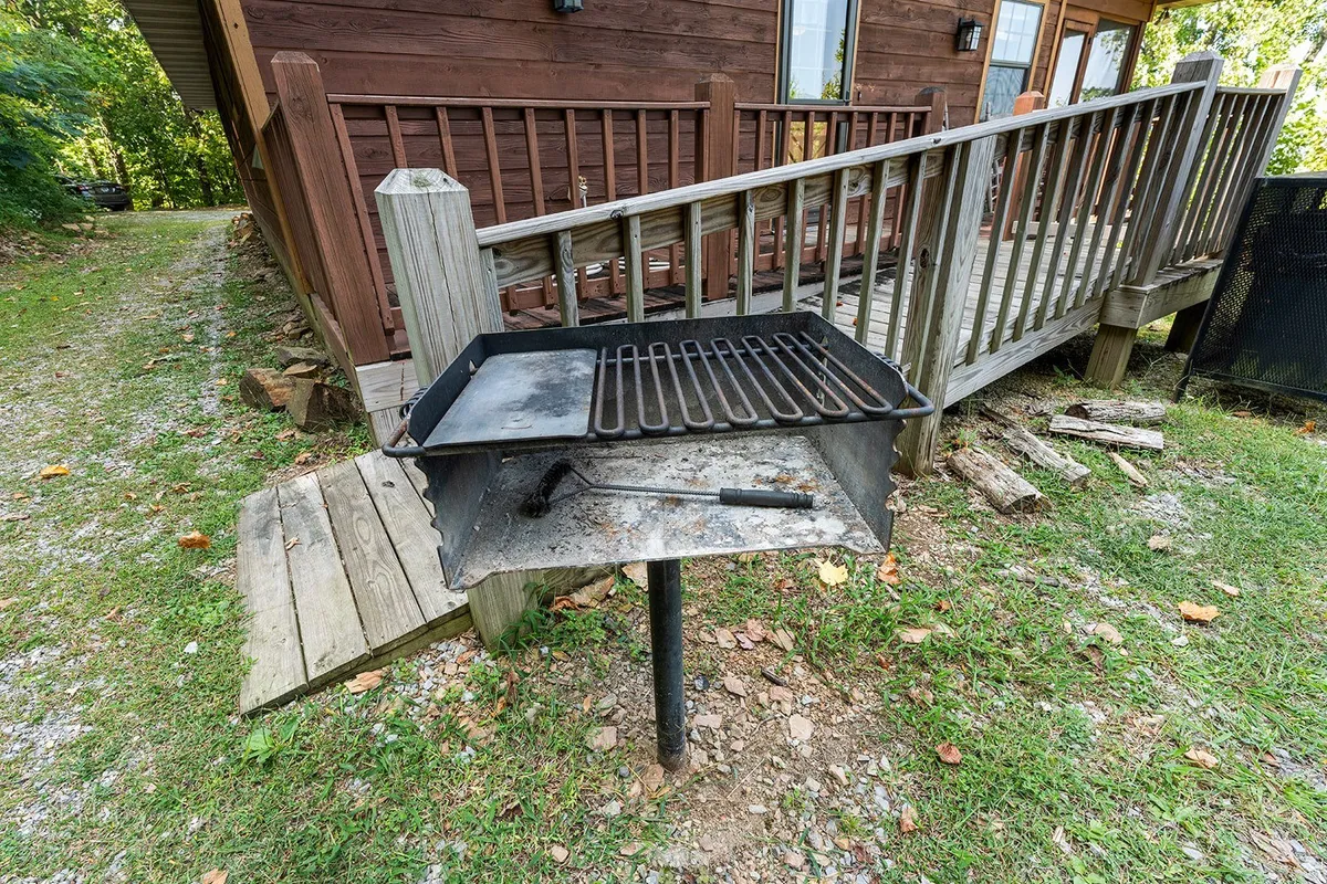 A wooden deck features a grill and outdoor dining area, with a walkway leading into the surrounding greenery. The setup is perfect for outdoor meals, socializing, and letting pets lounge close by while the family enjoys barbecue evenings.