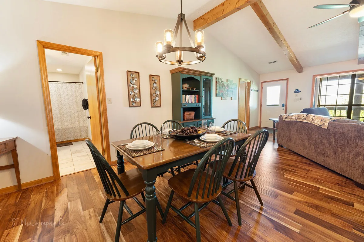 A warm and welcoming dining room centered around a rustic wooden table and chandelier, set against wooden beams and a stylish blue cabinet. The setup encourages family dinners, game nights, and memorable moments shared indoors.