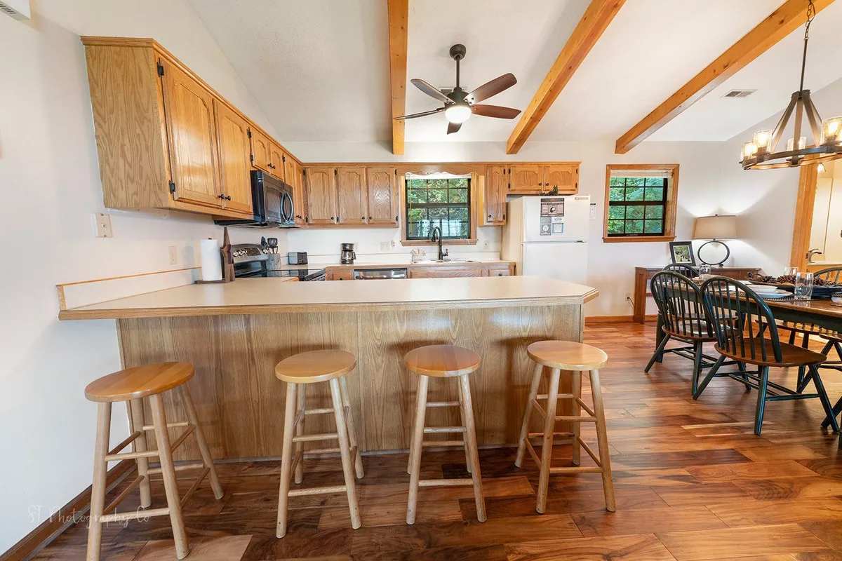 This image features an inviting kitchen and dining area with a central island, warm wooden cabinets, and a dining table set for shared meals. The space is bathed in natural light, offering an atmosphere perfect for family gatherings or entertaining guests.