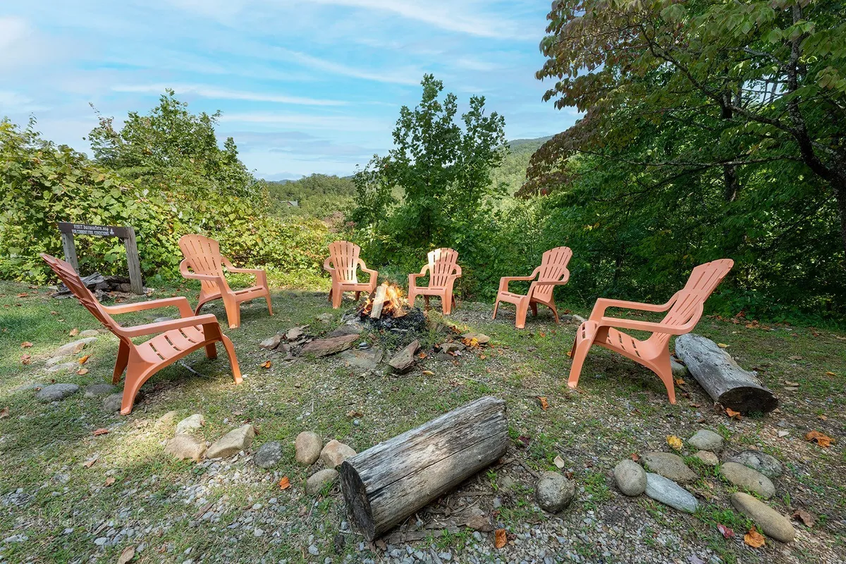 This outdoor scene features a fire pit surrounded by Adirondack chairs, set against a backdrop of greenery. The arrangement invites guests to gather for s’mores, stories, or simply unwinding beneath the stars after a day spent exploring local attractions.
