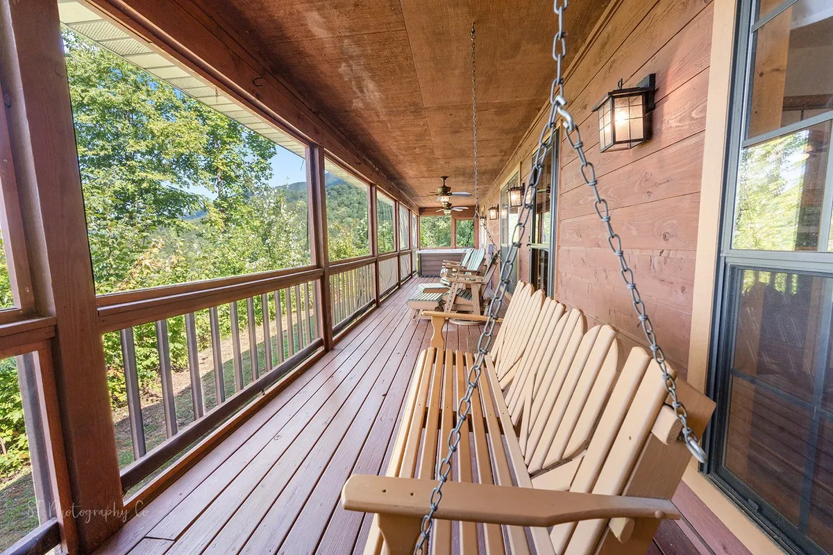 An interior shot of a screened porch with swinging chairs and expansive windows that showcase the natural beauty outside. The space feels intimate and tranquil, perfect for couples seeking quiet time together while still staying connected to the outdoors.