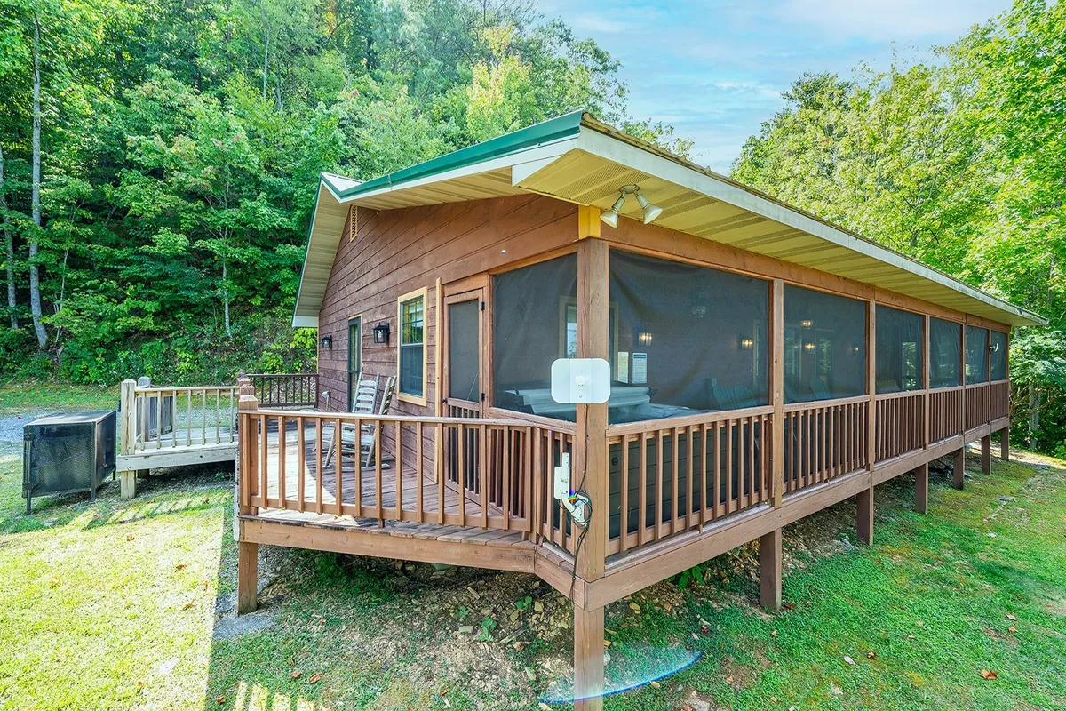 This image showcases a spacious wooden deck and a screened porch surrounded by lush greenery. The seating areas invite guests to relax and enjoy the natural beauty, with plenty of space for both people and pets. The setting suggests peaceful mornings, stargazing nights, and a seamless connection to the outdoors.