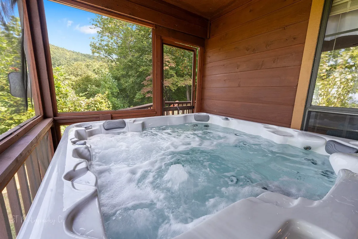 A bubbling hot tub sits beside large windows, offering views of surrounding greenery. The tranquil space blurs the line between indoors and outdoors, promising relaxation after an active day. Sunlight streams in, highlighting the inviting, restorative atmosphere ideal for unwinding muscles post-hike.