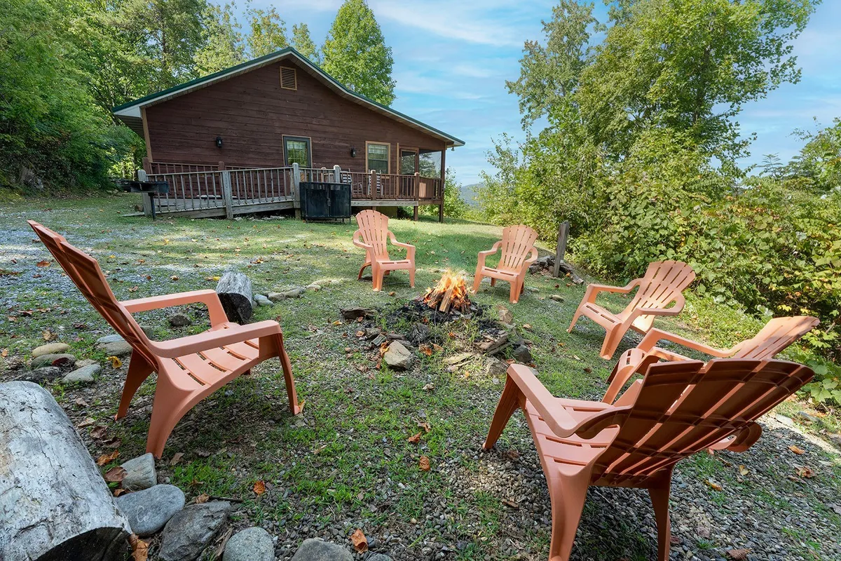 The exterior features a warm fire pit surrounded by Adirondack chairs, nestled among trees with the cabin in view. The space evokes a sense of outdoor freedom, inviting guests and their dogs to gather, play, or relax in nature together.