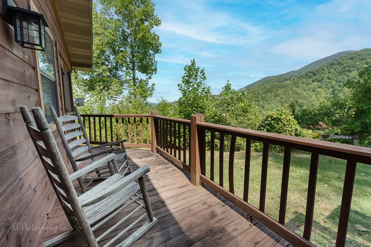 A wide wooden porch with rocking chairs overlooks a striking mountain view and lush greenery. The space is tranquil and inviting, ideal for peaceful mornings or sharing time outdoors with pets and family. The natural setting is serene, offering an immersive mountain experience.